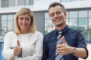 Free photo two happy male and female business people showing thumbs up outdoors.