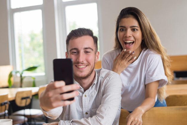 Two happy male and female students videoconferencing in cafe