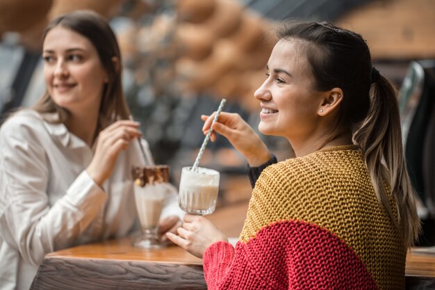 Free photo two happy women are sitting in a cafe, drinking milkshakes,