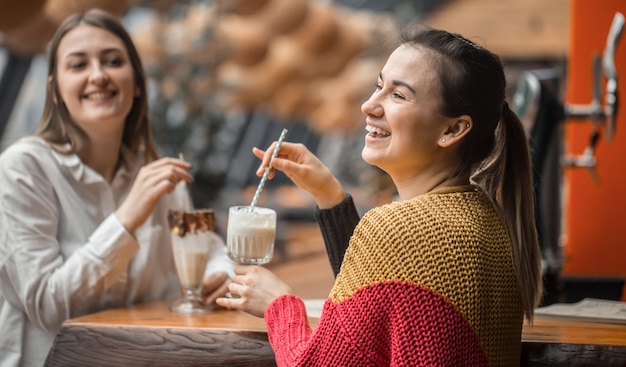 Free photo two happy women are sitting in a cafe, drinking milkshakes,