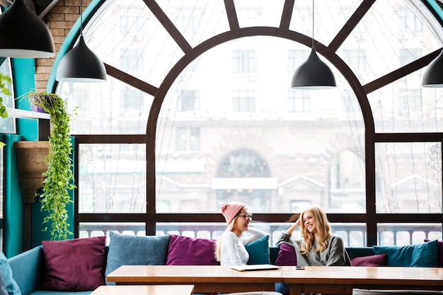 Free photo two happy women sitting and talking in cafe