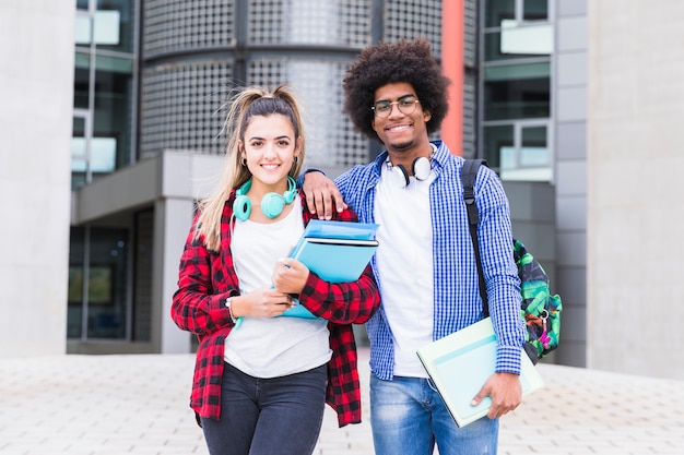 Two happy young students looking to camera standing in front of university building