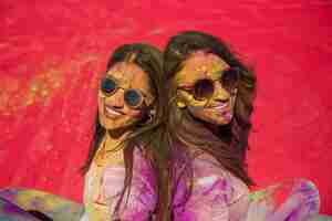 Free photo two happy young women covered with holi color sitting back to back