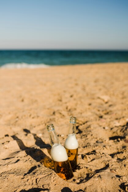 Two ice cold beer bottles in the sand under the bright sun at beach