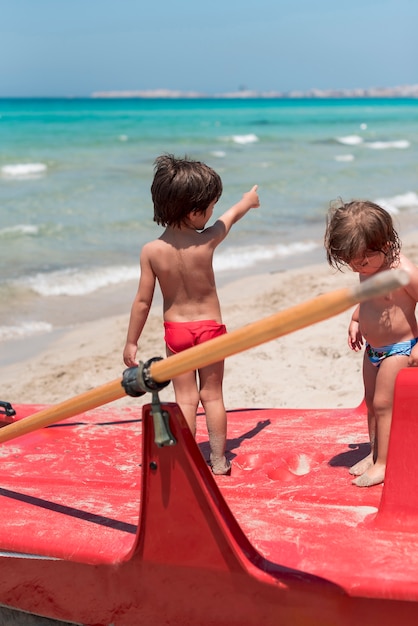 Free photo two kids at the beach standing on paddle boat