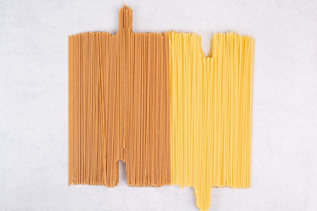 Two kinds of raw spaghetti pasta on white surface