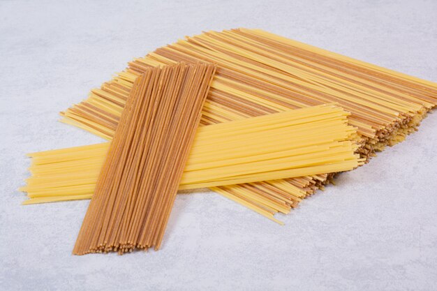 Two kinds of raw spaghetti pasta on white surface