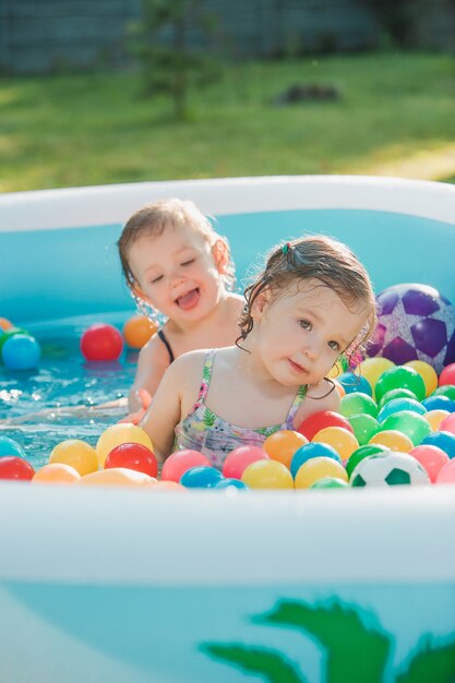 The two little baby girls playing with toys in inflatable pool in the summer sunny day