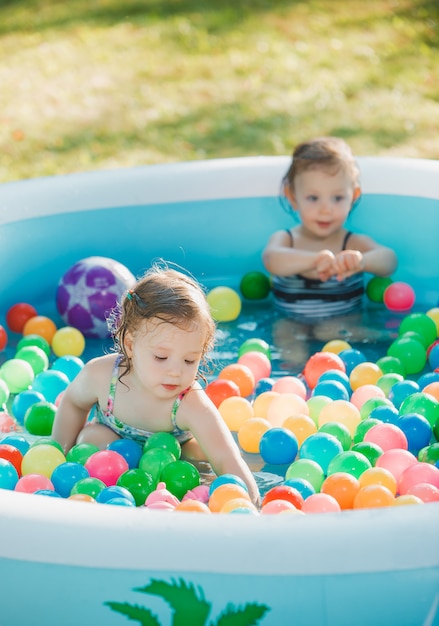 The two little baby girls playing with toys in inflatable pool in the summer sunny day