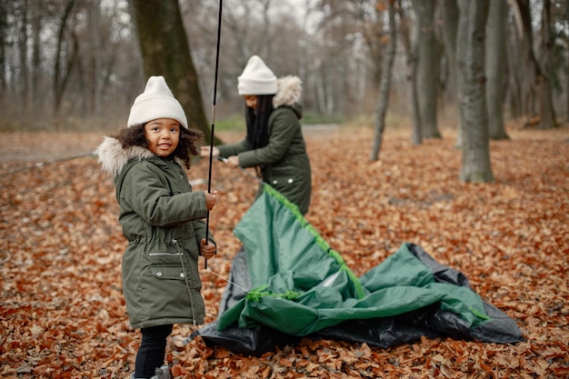 Free photo two little black girls in tent camping in the forest two little sisters are puting up a tent in autumn forest black girls wearing khaki coats and beige hats