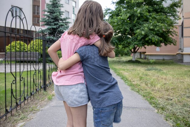 Two little girlfriends sisters hug on a walk in the summer