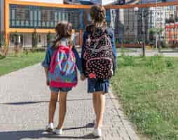 Free photo two little girls go to school, holding hands, back view.