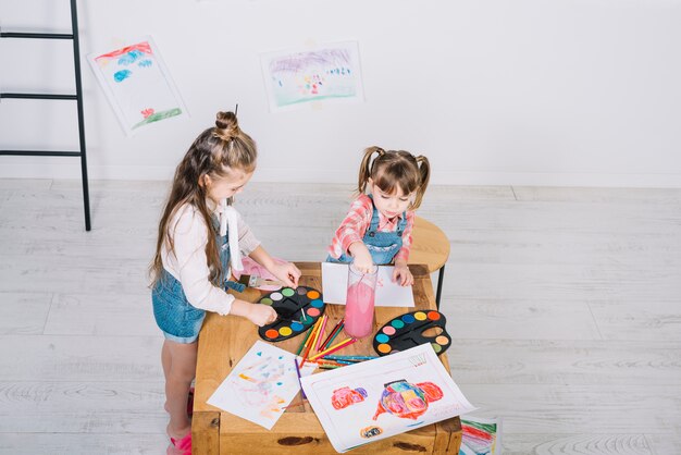 Two little girls painting with aquarelle at wooden table