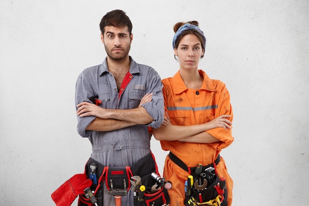 Free photo two maintenance workers stand next to each other, keep hands folded, raise eyebrows in bewilderment,