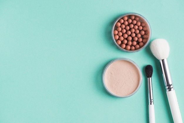 Two makeup brush with compact and bronzed pearls over green backdrop