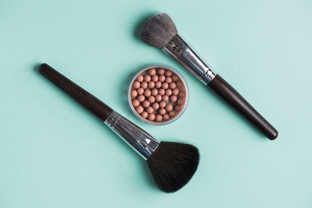 Two makeup brushes with bronzed pearls over green background