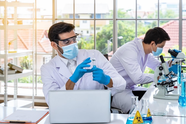 Free photo two male asian and arab researcher scientists working in laboratory conducting study biohazard substance with scientific equipment and microscope