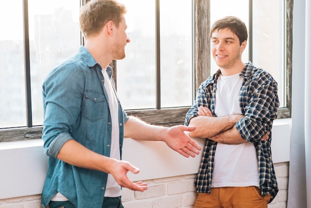 Free Photo two male friends standing near the window talking to each other