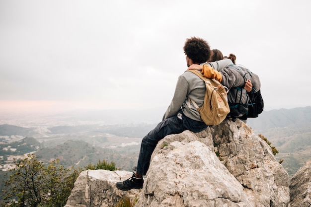 Free photo two male hiker sitting on top of rock over the mountain looking at scenic view