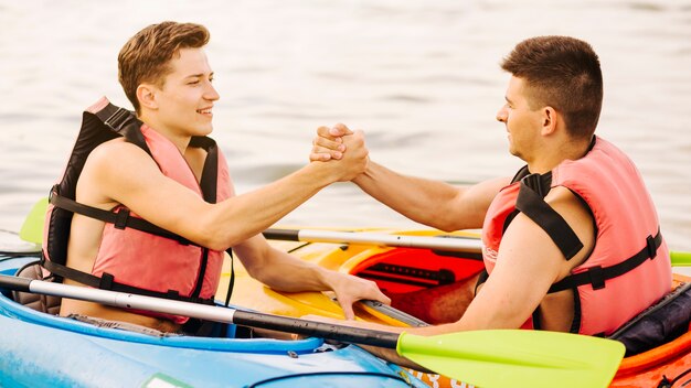 Two male kayaker sitting face to face holding each other's hand