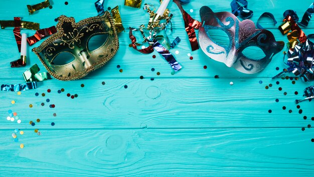 Two masquerade carnival mask with party decorations over blue wooden table