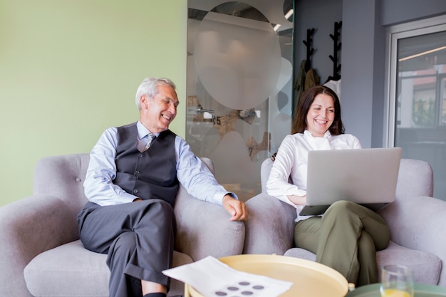 Two mature businessman looking at businesswoman using laptop in the office