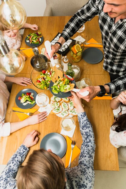 Two men putting tasty dish on plate for women and little girl