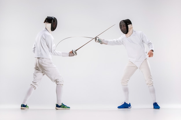 Free photo the two men wearing fencing suit practicing with sword against gray