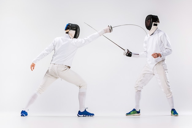 The two men wearing fencing suit practicing with sword against gray