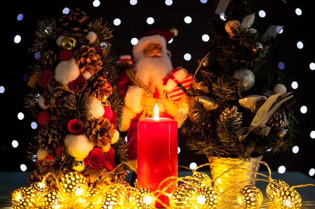 Two mini christmas trees and a santa claus figurine on black background with bokeh lights on it