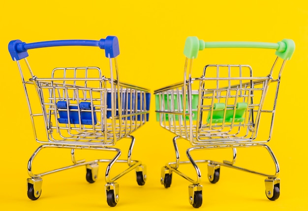 Free photo two miniature green and blue shopping cart on yellow background