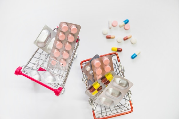 Free photo two miniature shopping carts filled with pills blister on white background