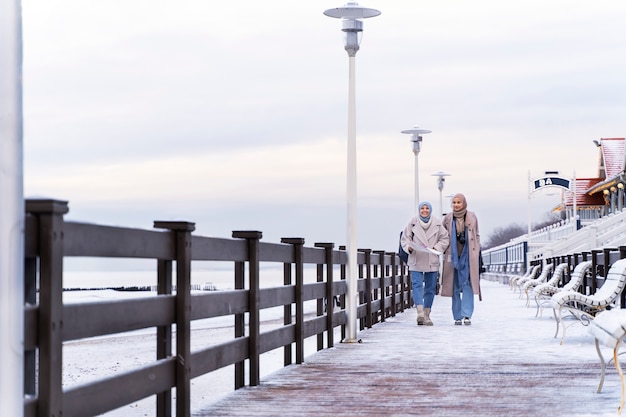 Free Photo two muslim women with hijabs consulting the map and walking by the ocean while traveling