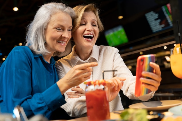 Two older female friends using a smartphone at a restaurant