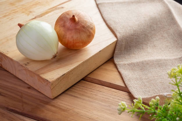 Two onions on a light brown wood cutting board.