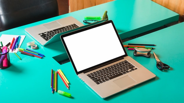 Two open laptop with colorful stationeries on turquoise table