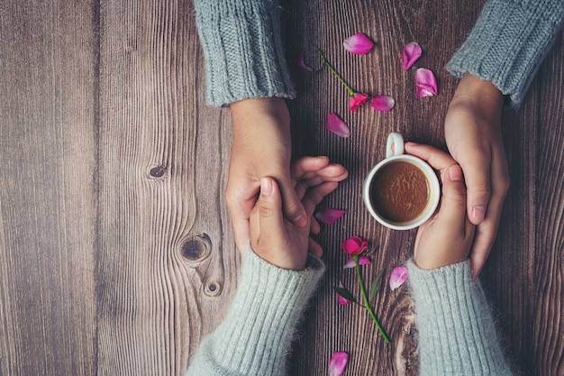 Free Photo two people holding cup of coffee in hands with love and warmth on wooden table