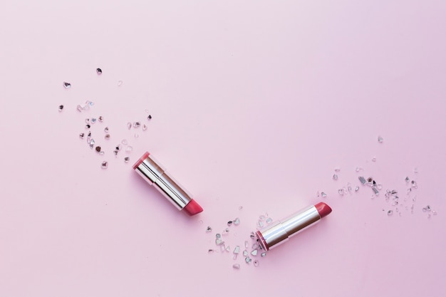 Free photo two pink lipsticks with crushed glass pieces on pink background