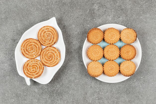 Two plates of sandwich cookies and biscuit with sesame seeds