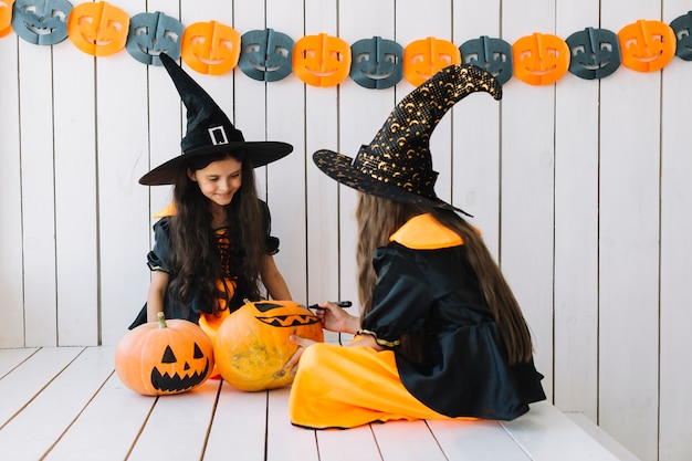 Free Photo two pretty halloween witches painting pumpkins