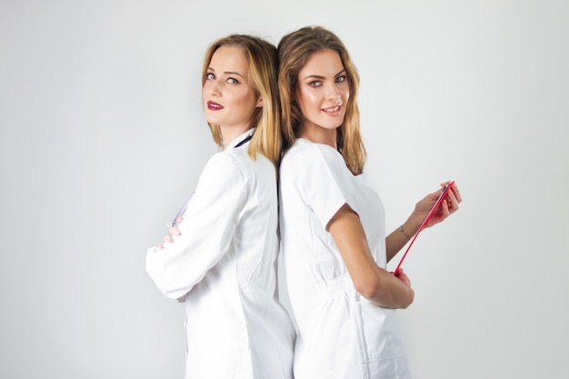 Two pretty young women doctors, nurses standing back to back in the hospital.