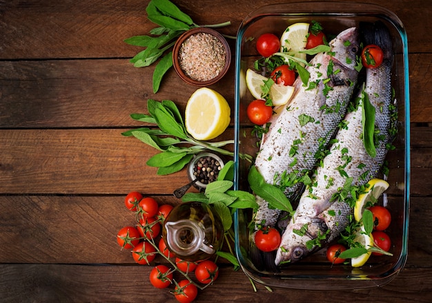 Two raw seabass in a baking dish with spices on an old wooden table. Top view