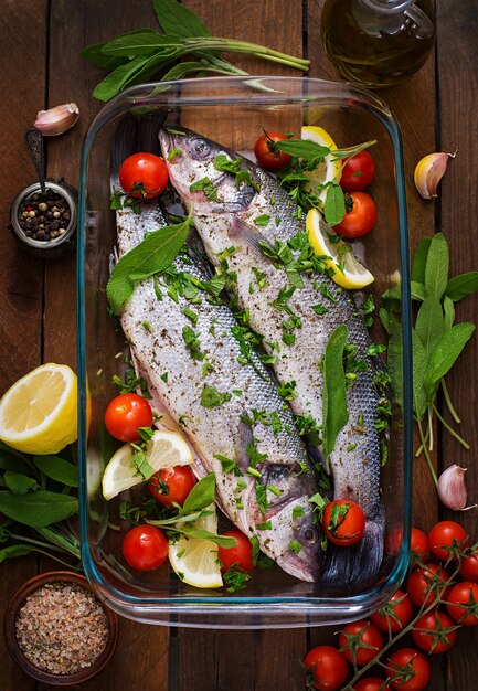 Two raw seabass in a baking dish with spices on an old wooden table. Top view