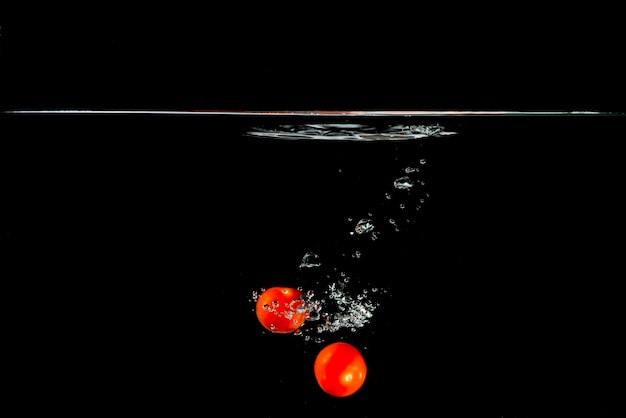 Free photo two red tomatoes falling in water against black background