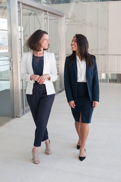 Two relaxed female colleagues walking in office hall