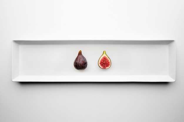 Free Photo two ripe fresh figs isolated in center rectangular ceramic plate on white table