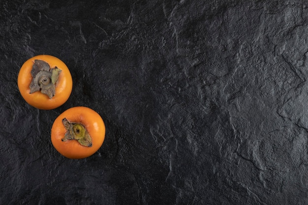 Free Photo two ripe persimmon fruit placed on black surface