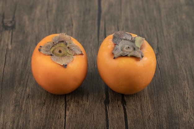 Free photo two ripe persimmon fruit placed on wooden surface