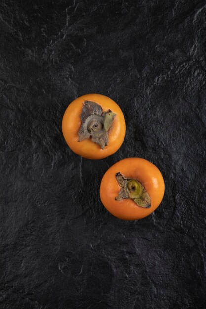 Two ripe persimmon fruits placed on black surface