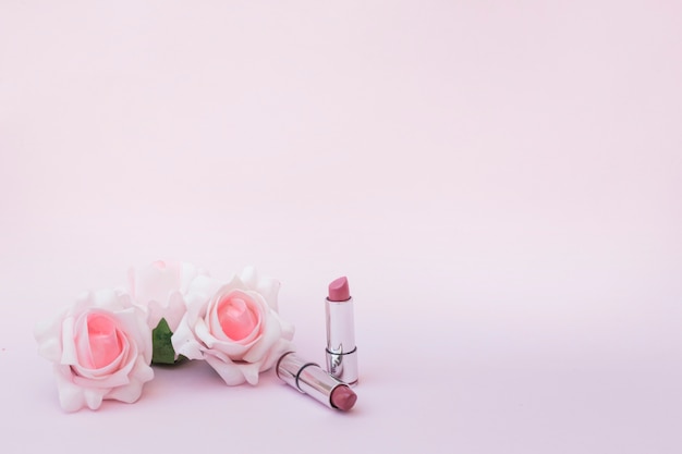 Two roses and lipsticks on pink backdrop